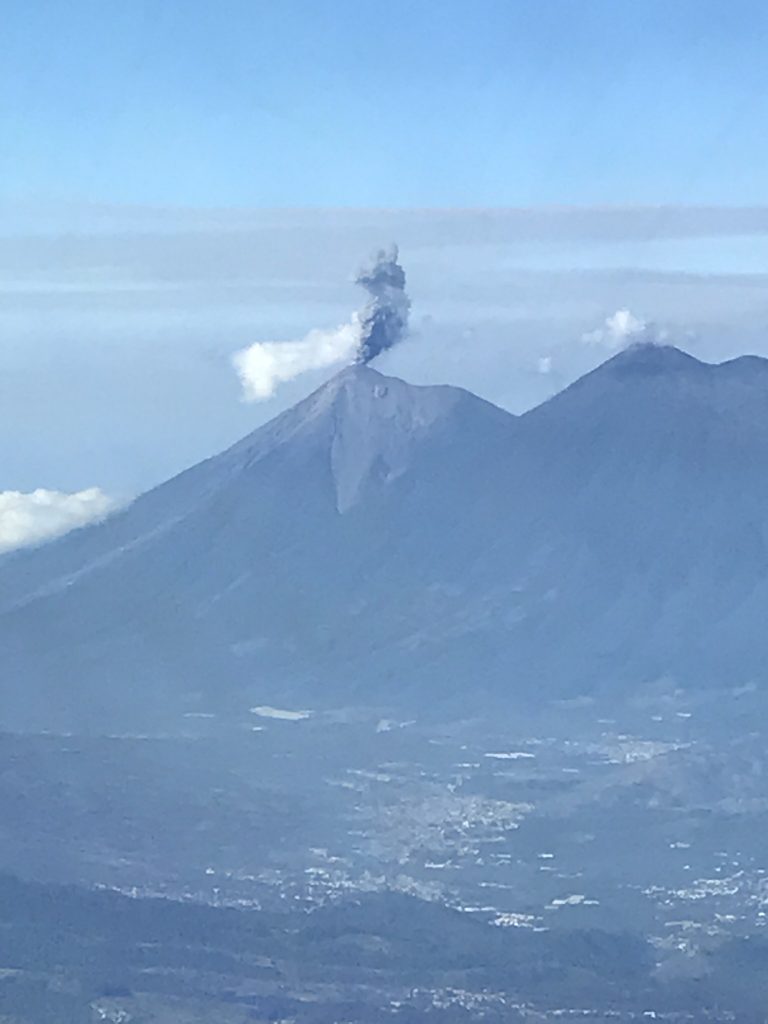 Photo of ash arising from the Guatemalan Volcán de Fuego, taken from the cockpit of a commercial airliner. Such spurts of ash are easily avoided by aviators, but if a large eruption begins suddenly, winds change, or an airplane is flying at night, these hazards become harder to see. Credit: Tom Gonzalez 